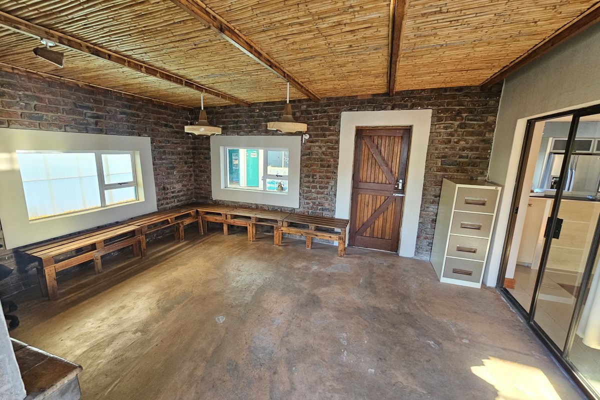 Spacious living area featuring exposed brick walls, a unique bamboo ceiling, and concrete flooring, offering a rustic aesthetic with direct access to adjacent spaces.