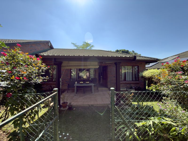 A view of the rear exterior featuring a covered patio with tiled flooring, brick facade, and a well-maintained garden area.