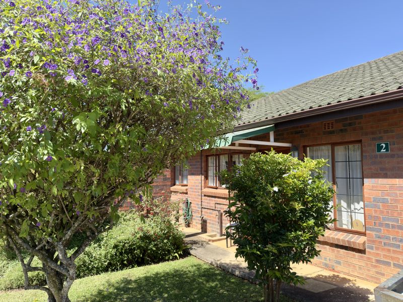 A view of the front brick facade of the property featuring a tiled roof, an awning, and a well-maintained garden area.