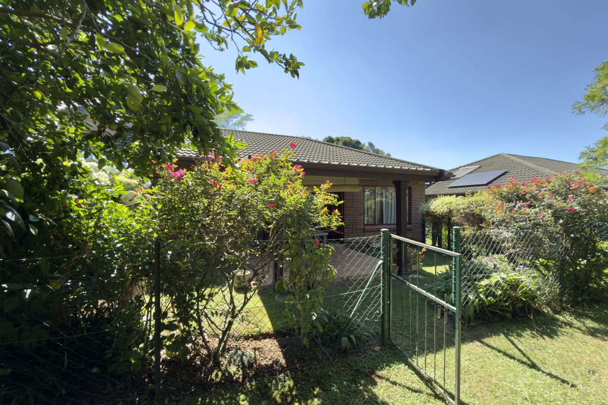 A view of the rear exterior of the house featuring a paved patio, brick facade, tiled roof with solar panels, and a fenced garden area.