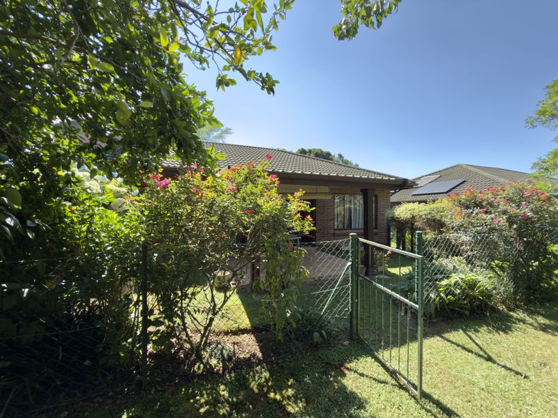 A view of the rear exterior of the house featuring a paved patio, brick facade, tiled roof with solar panels, and a fenced garden area.