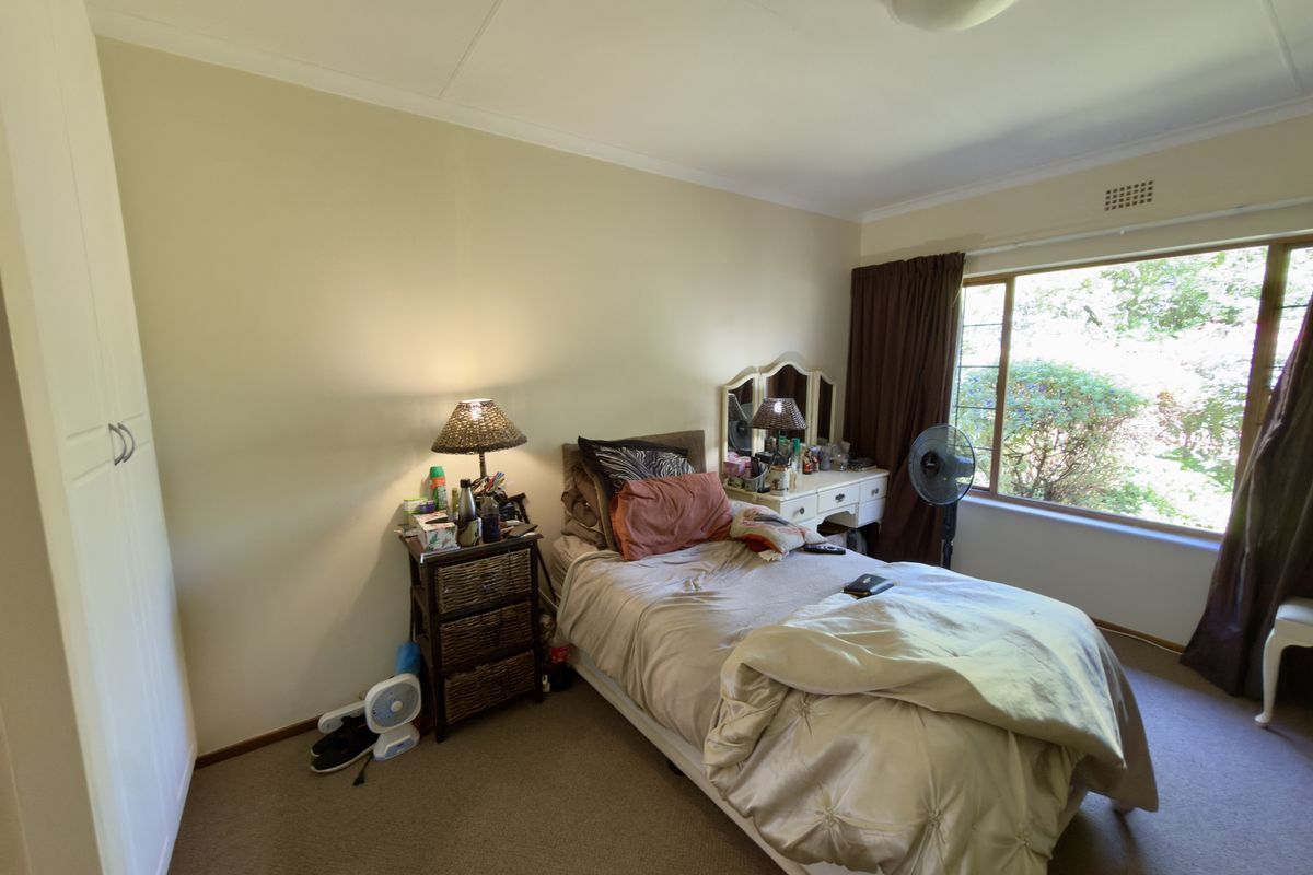 A functional bedroom featuring carpeted flooring, a built-in wardrobe, and a large window providing natural light and garden views.
