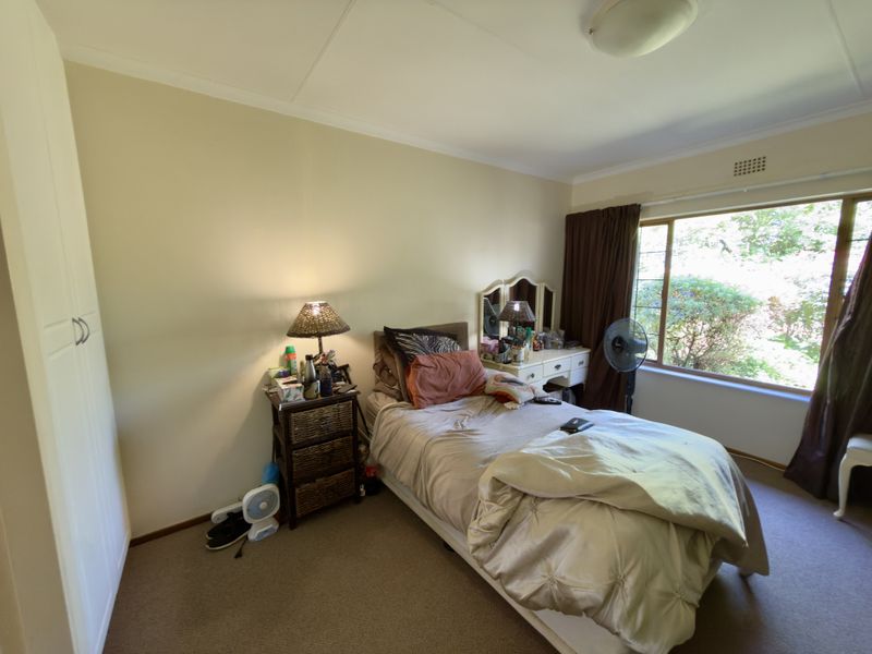 A functional bedroom featuring carpeted flooring, a built-in wardrobe, and a large window providing natural light and garden views.