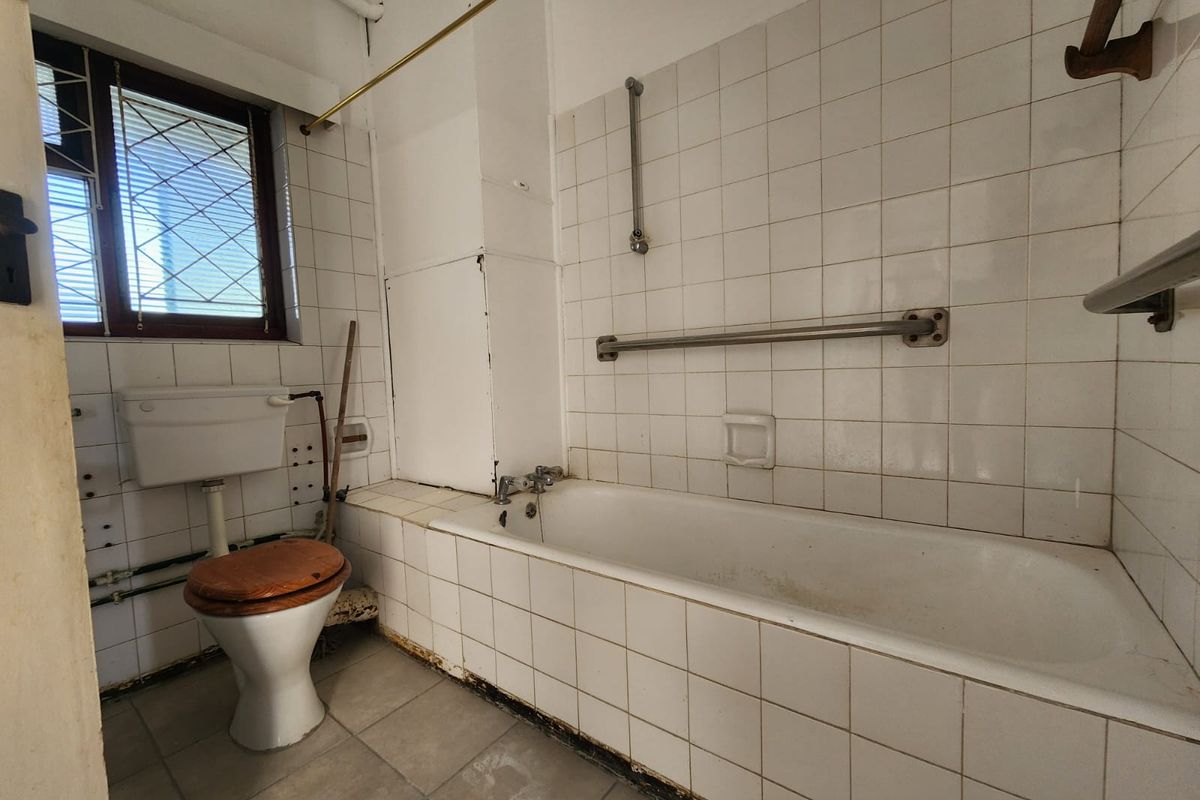 A dated bathroom featuring a standard bathtub, toilet, and tiled walls. The space requires significant renovation and modernization of fixtures and finishes.