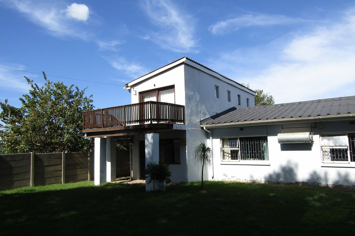 Rear view of the property featuring a raised balcony with timber balustrade, metal roofing, and a private garden area with boundary walling.