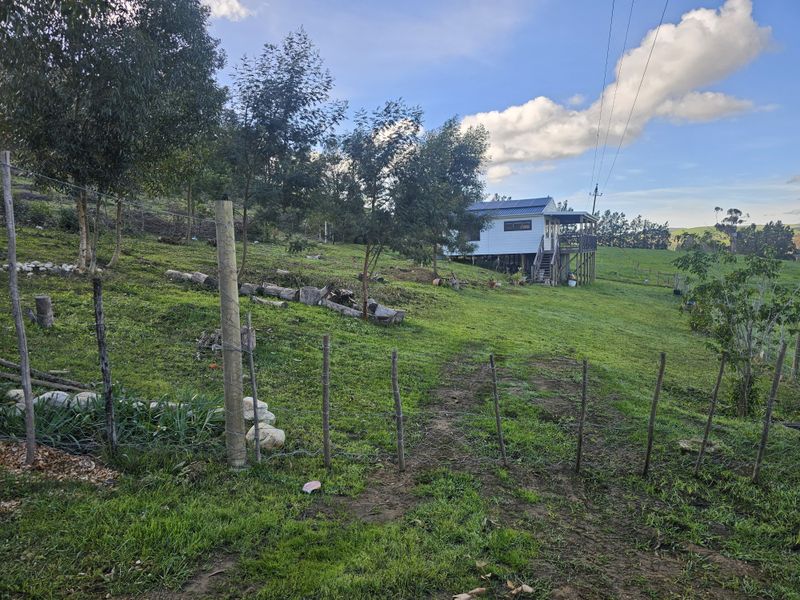 A view of the rear elevation of the farm dwelling, featuring a raised timber deck and metal roofing set within a grassy landscape.