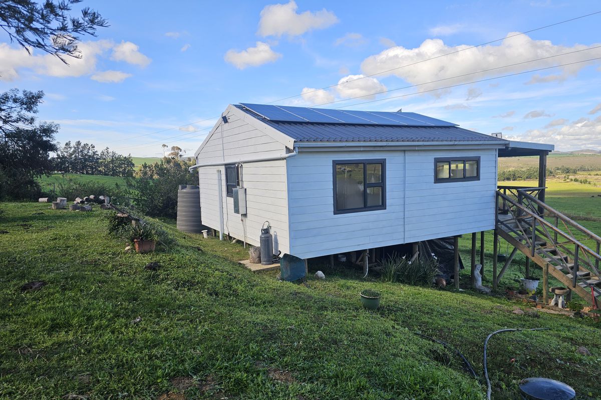 Rear view of a farm dwelling featuring a raised timber deck, metal roofing with integrated solar panels, and a water storage tank.