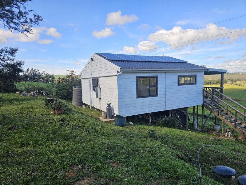 Rear view of a farm dwelling featuring a raised timber deck, metal roofing with integrated solar panels, and a water storage tank.