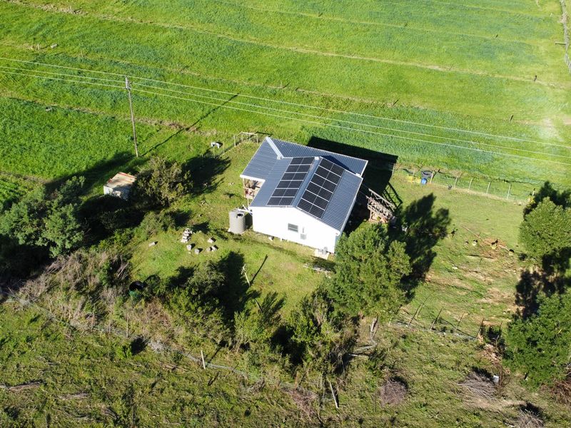 Aerial view of a rural farm property featuring a house with a metal roof, installed solar panels, and surrounding agricultural land.
