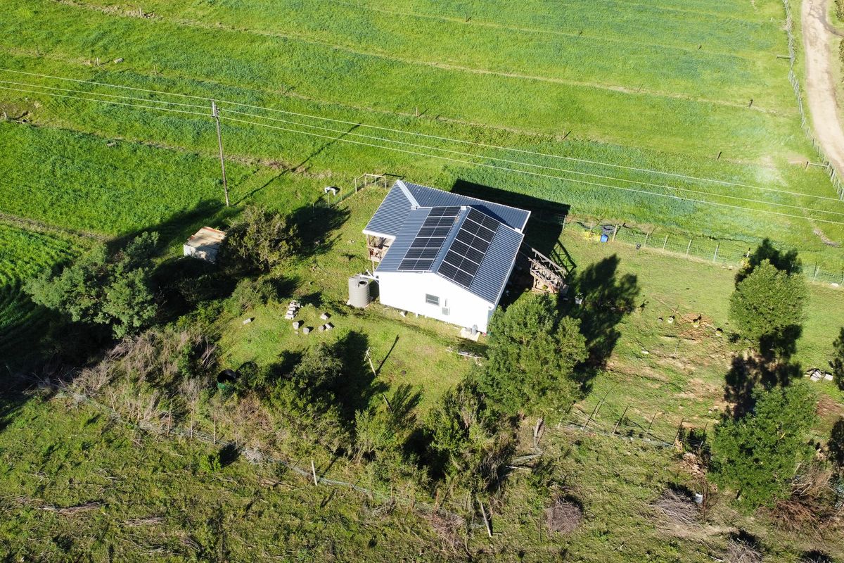 Aerial view of a rural farm property featuring a house with a metal roof, installed solar panels, and surrounding agricultural land.