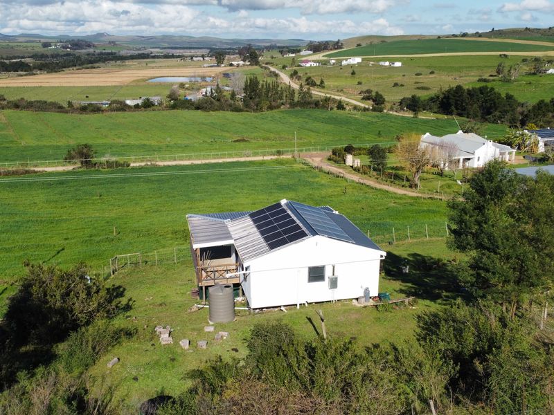 Aerial view of a farm property featuring a dwelling with a solar panel array, a water tank, and an attached timber deck.