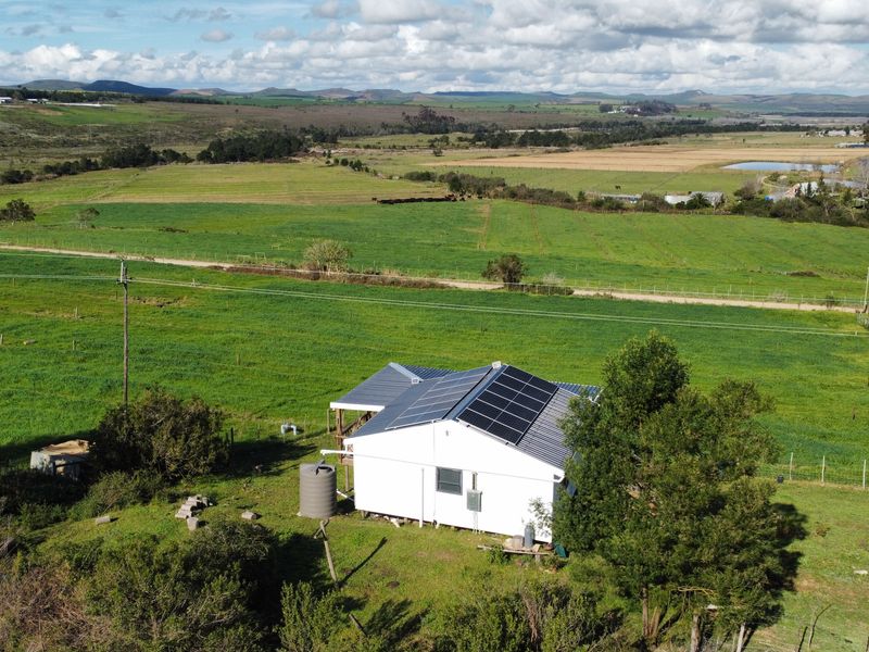 Aerial view of a rural farm property featuring a white building with a metal roof, solar panel installation, and an adjacent water storage tank.