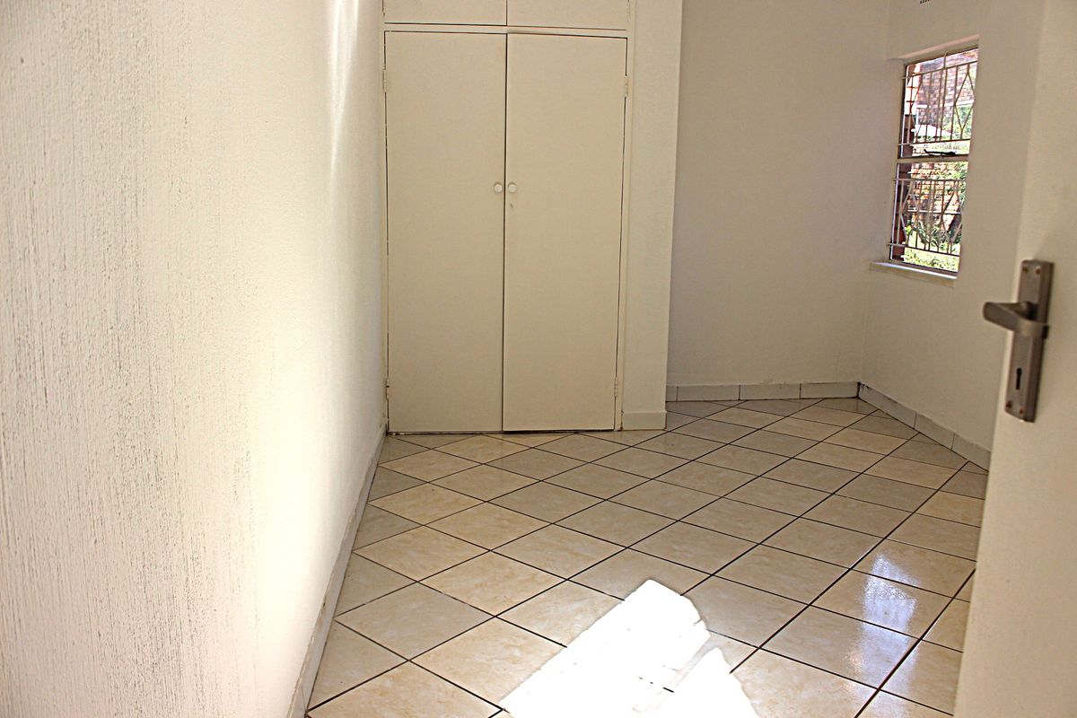 An empty bedroom featuring tiled flooring, a built-in wardrobe, and a window with security bars.