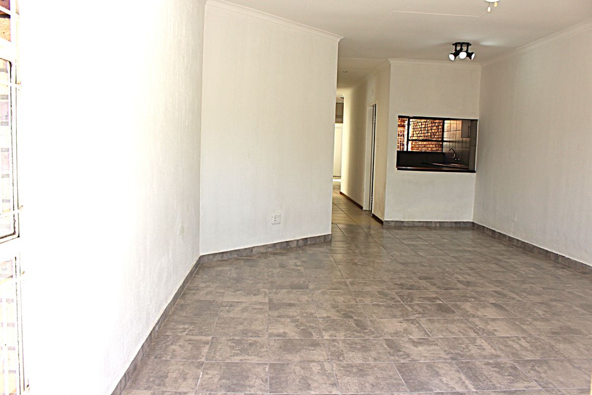 An empty, open-plan living area featuring neutral tiled flooring, coved ceilings, and a convenient pass-through window connecting to the kitchen space.