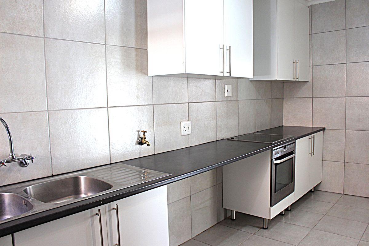 A clean, functional kitchen featuring white cabinetry, dark laminate countertops, built-in oven, electric hob, and neutral ceramic wall and floor tiling.