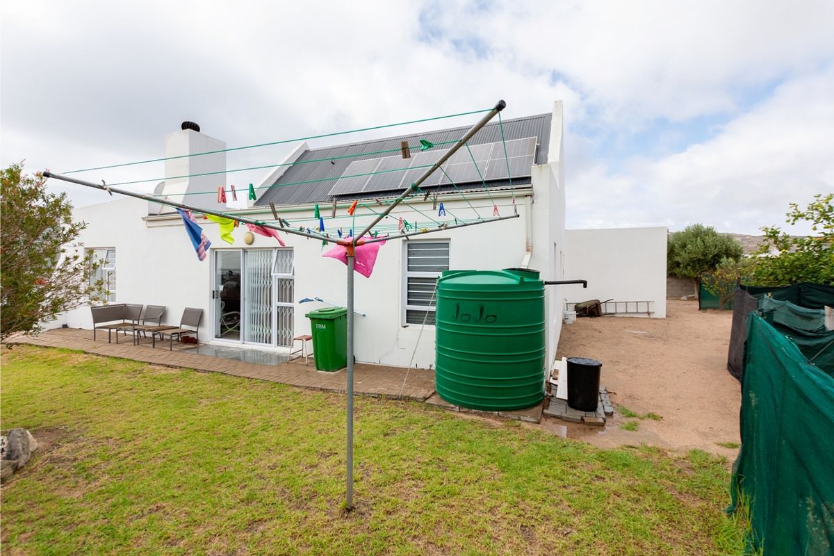 Rear view of the property featuring a paved patio, solar panels on the roof, and a large water tank in the garden area.