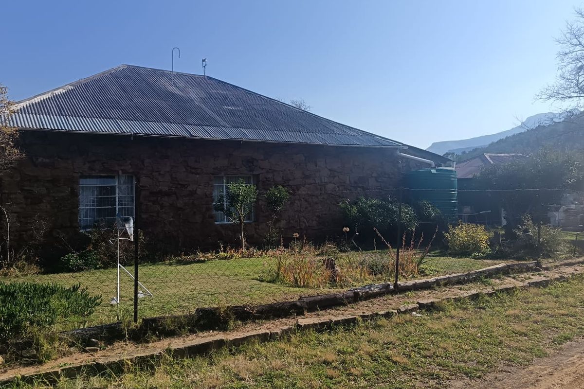 Rear view of a stone-walled house featuring a corrugated metal roof, guttering system, and an attached water storage tank set within a garden area.