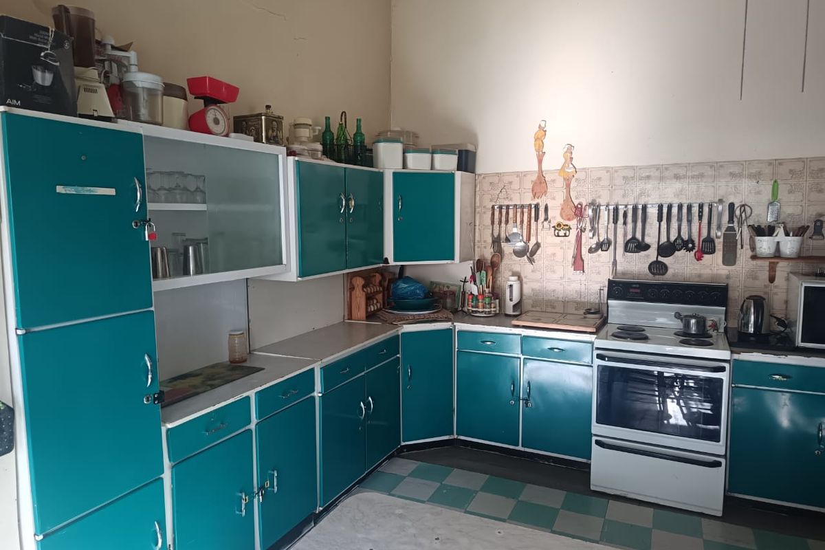 A vintage-style kitchen featuring teal cabinetry, tiled backsplash, and a freestanding stove, offering significant potential for a modern renovation.