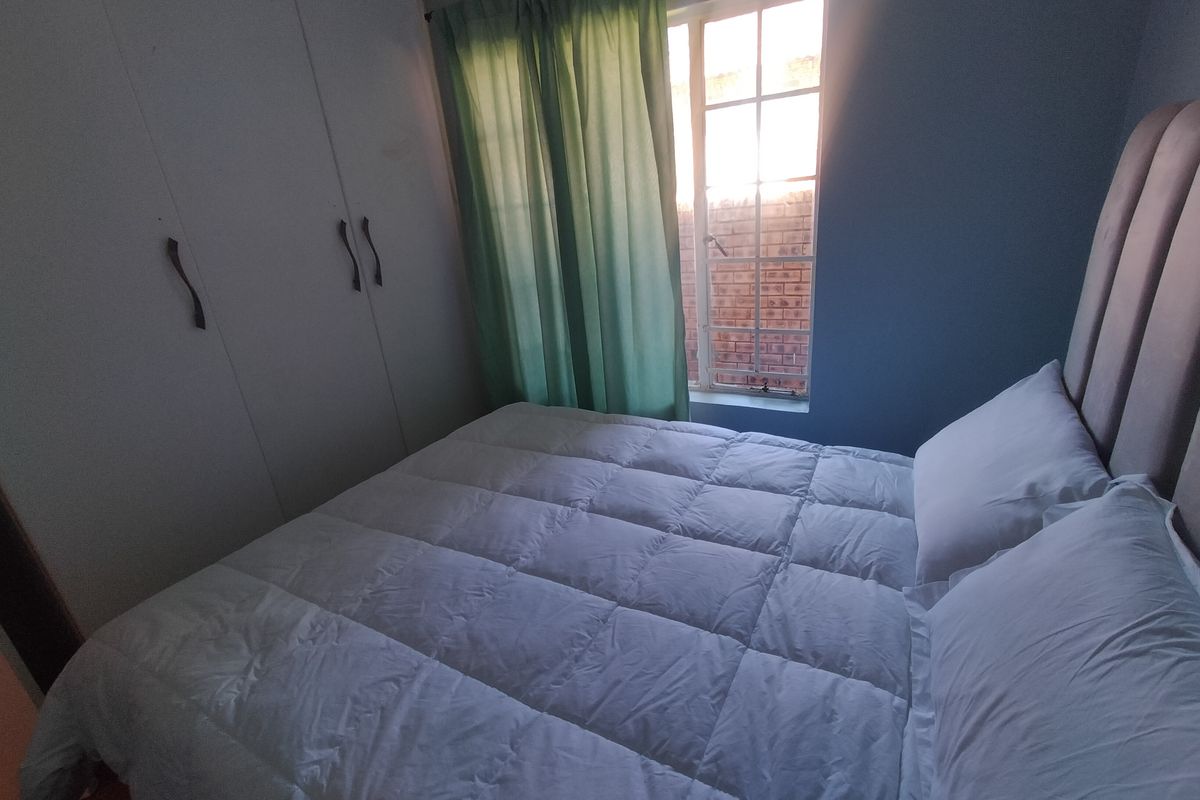 A bedroom featuring built-in cupboards and a steel-framed window, providing a functional space with natural light.