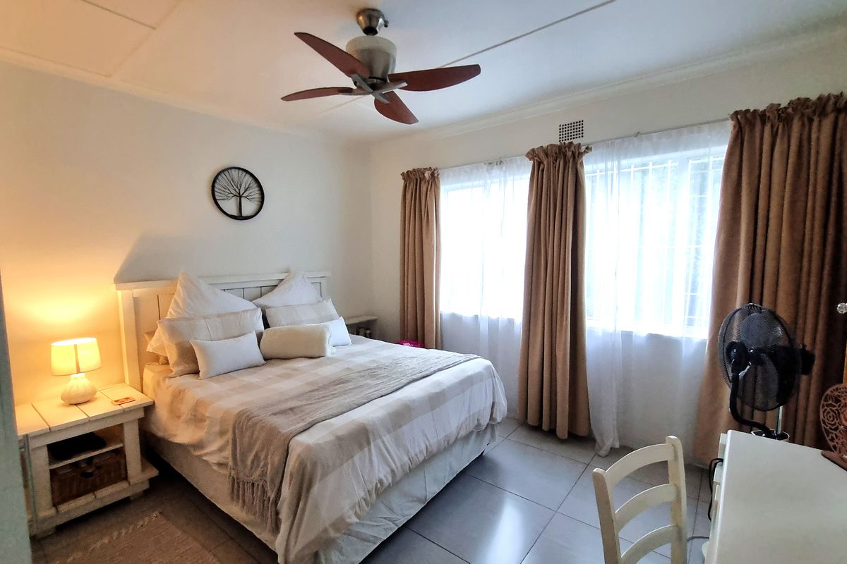A well-lit bedroom featuring tiled flooring, a ceiling fan, and built-in storage, offering a comfortable and functional living space.