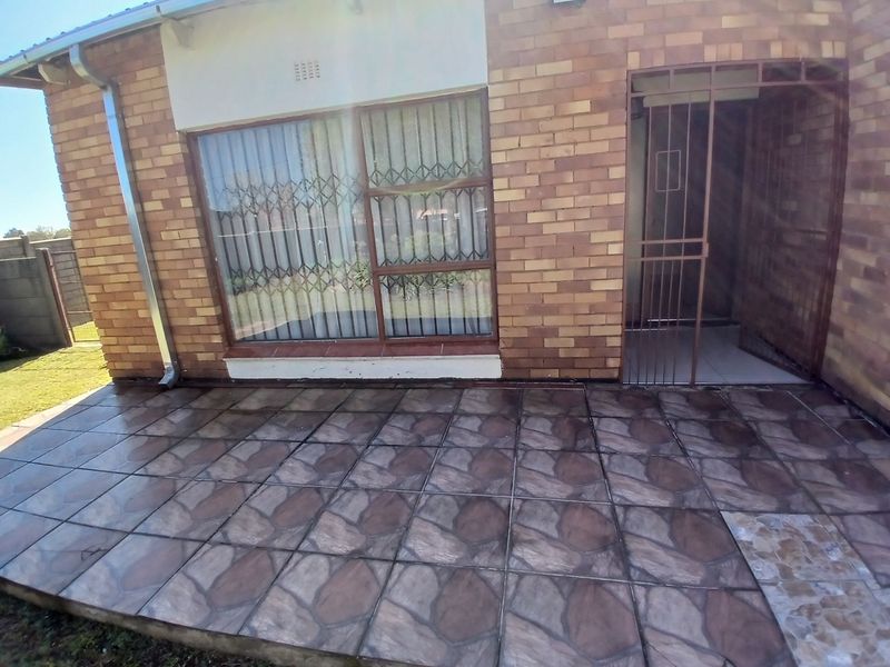 A paved outdoor patio area featuring brick exterior walls, security gates, and protective window bars, providing a functional space for outdoor relaxation.
