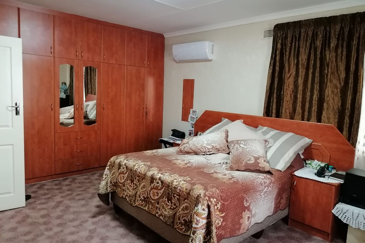A bedroom featuring built-in wooden cupboards, carpeted flooring, and a wall-mounted split-system air conditioning unit.
