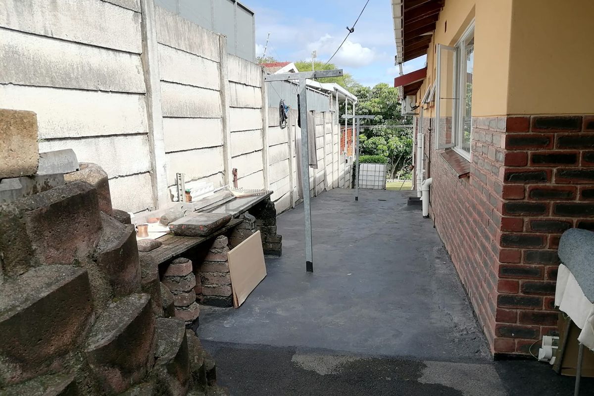 A narrow rear exterior side passage featuring concrete paving, a precast boundary wall, and brick exterior walling.