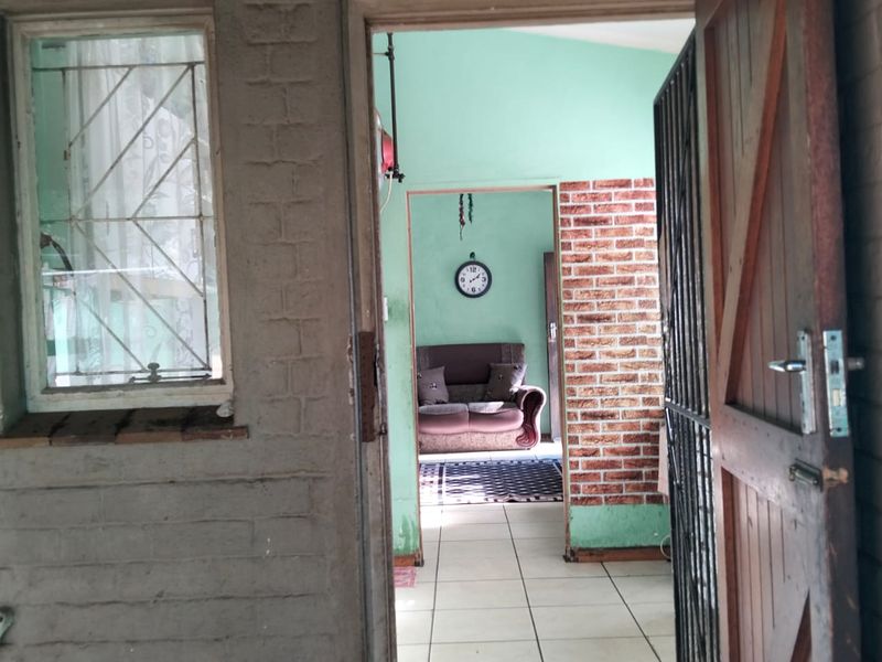 A view through a doorway into a living area featuring tiled floors, an exposed brick wall, and painted interior walls.