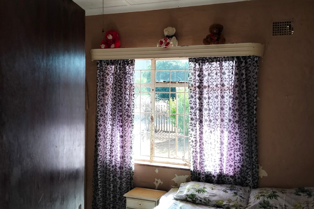 A bedroom featuring a ceiling fan, security bars on the window, and visible wall surface deterioration requiring maintenance and cosmetic updates.
