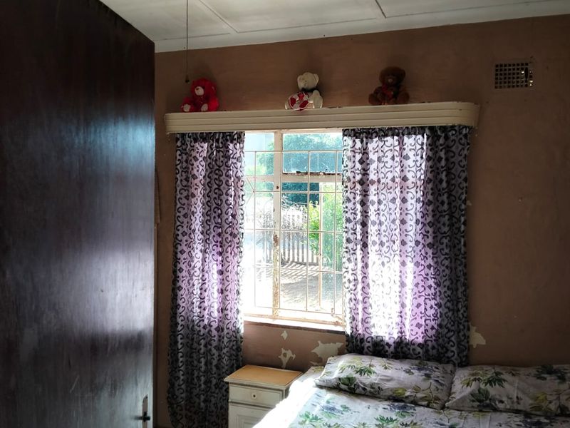A bedroom featuring a ceiling fan, security bars on the window, and visible wall surface deterioration requiring maintenance and cosmetic updates.