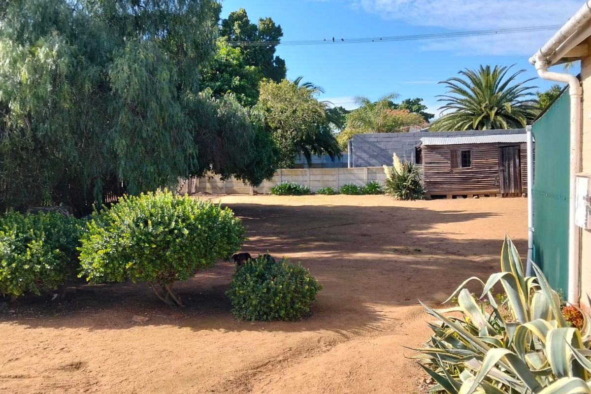 A spacious rear garden area featuring a large open yard, perimeter walling, and a detached wooden storage shed.