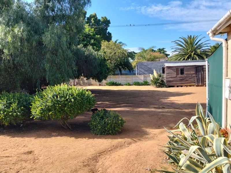 A spacious rear garden area featuring a large open yard, perimeter walling, and a detached wooden storage shed.