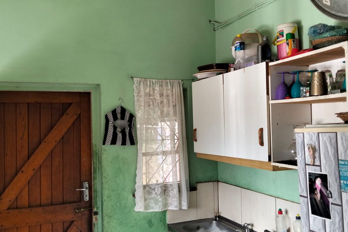 A compact kitchen area featuring a stainless steel sink, wall-mounted cabinetry, and a tiled splashback, requiring cosmetic updates to the wall finishes.