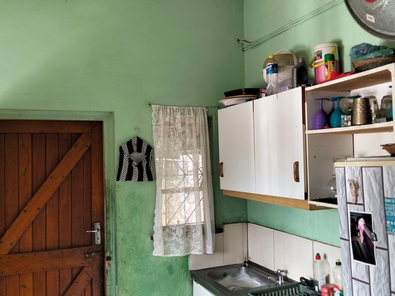 A compact kitchen area featuring a stainless steel sink, wall-mounted cabinetry, and a tiled splashback, requiring cosmetic updates to the wall finishes.