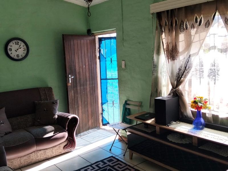 A living room featuring tiled flooring and a timber entrance door, requiring cosmetic updates to the wall finishes and general maintenance.