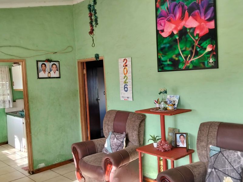 A living room area featuring tiled flooring and a ceiling fan, showing signs of wear on the wall surfaces.