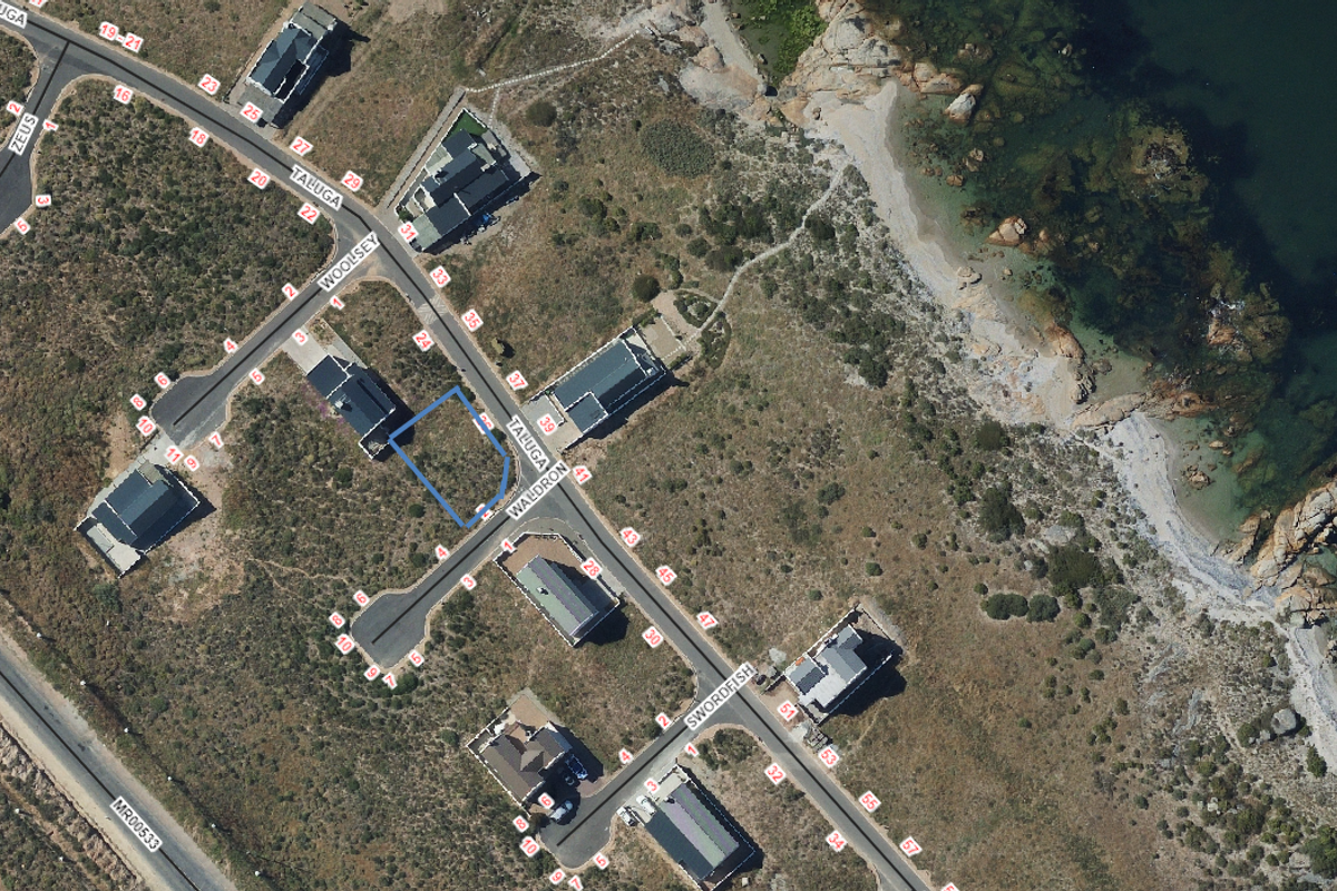 Aerial view of a vacant residential plot situated in a coastal estate with direct road access and proximity to the shoreline.