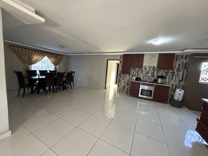 Open-plan living and dining area featuring tiled flooring and a functional kitchen with built-in cabinetry, oven, and hob.