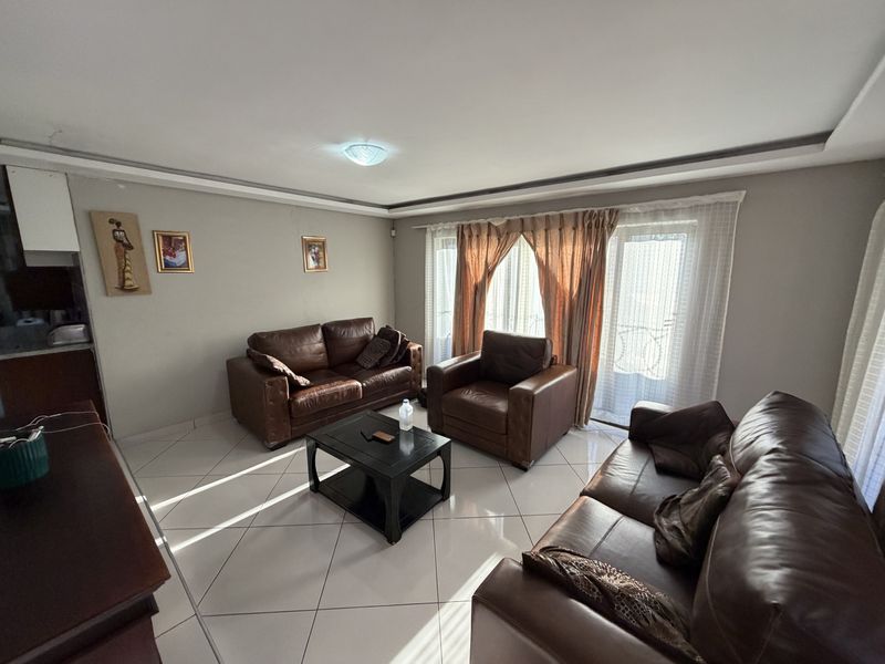 A spacious living room featuring tiled flooring, neutral wall tones, and a sliding glass door providing access to the exterior.