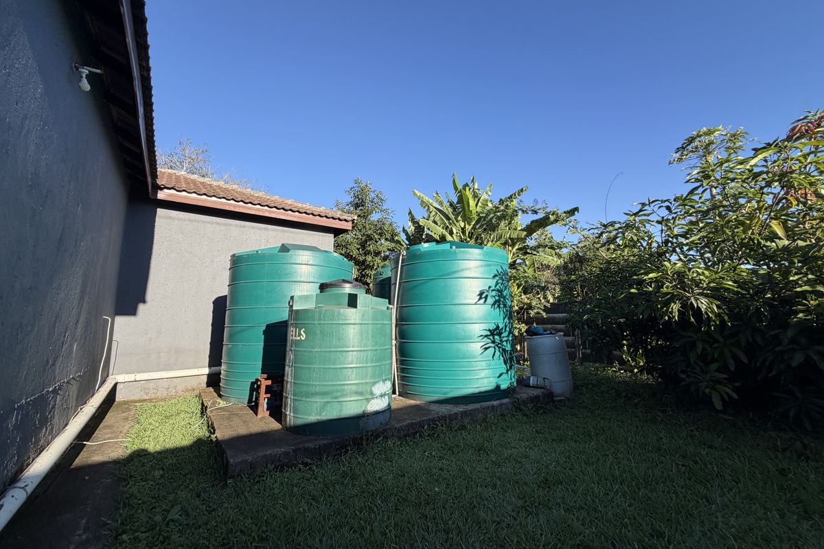 Rear exterior area featuring multiple green water storage tanks mounted on a concrete base alongside the house structure.