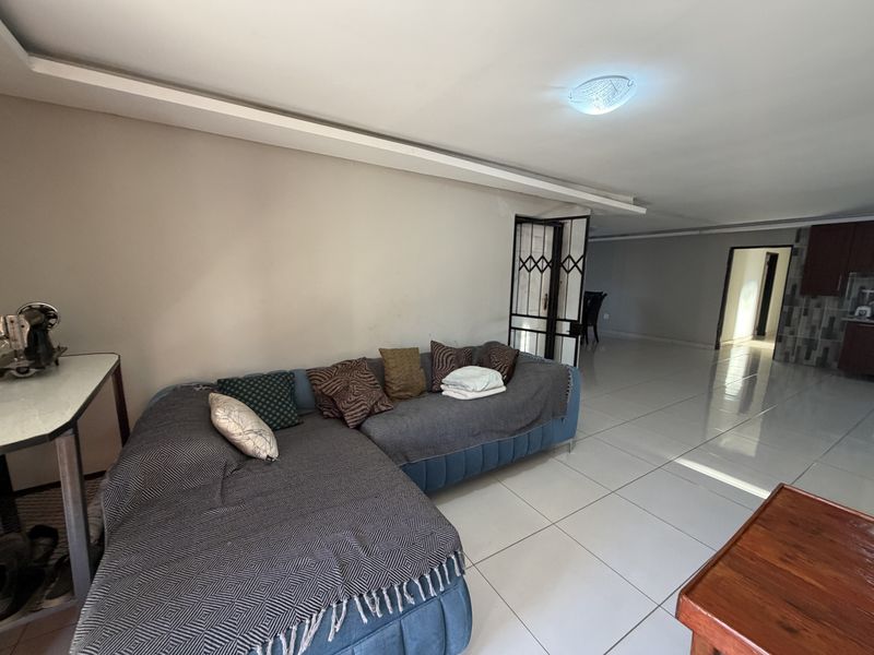 Open-plan living area featuring large format floor tiles, recessed ceiling detail, and a security gate leading to the entrance.