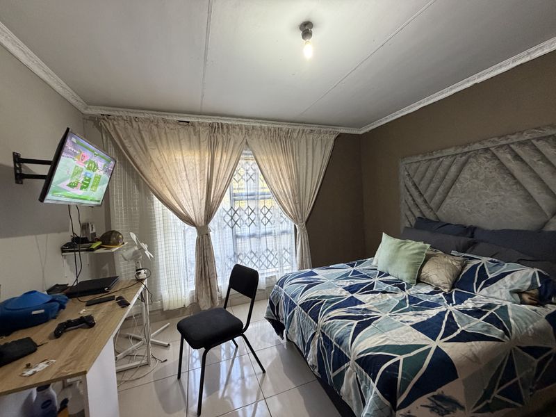 A bedroom featuring tiled flooring, decorative ceiling cornices, and a window fitted with a security gate.