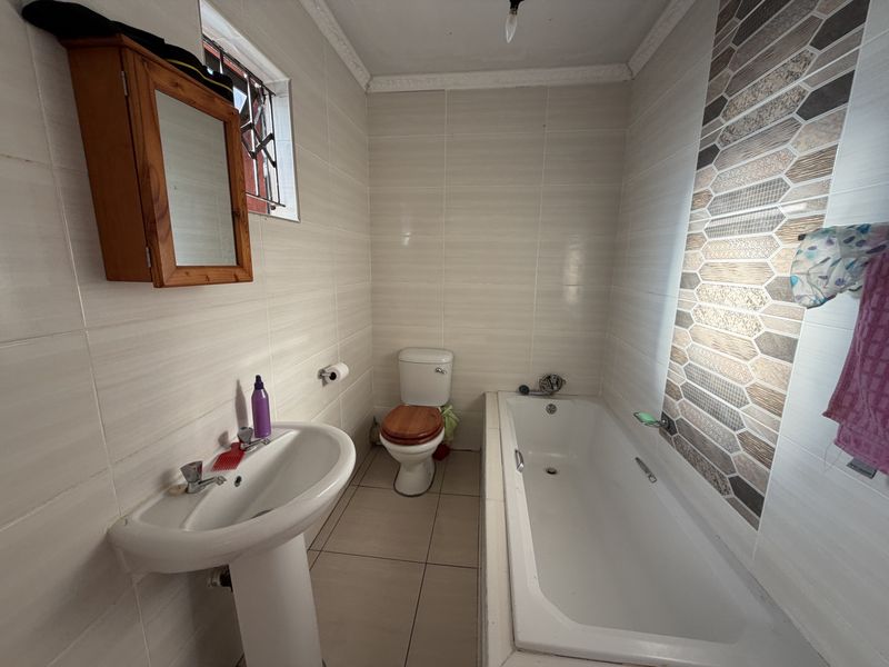 A functional bathroom featuring a pedestal basin, standard bathtub, and toilet with neutral wall tiling and a decorative mosaic feature wall.