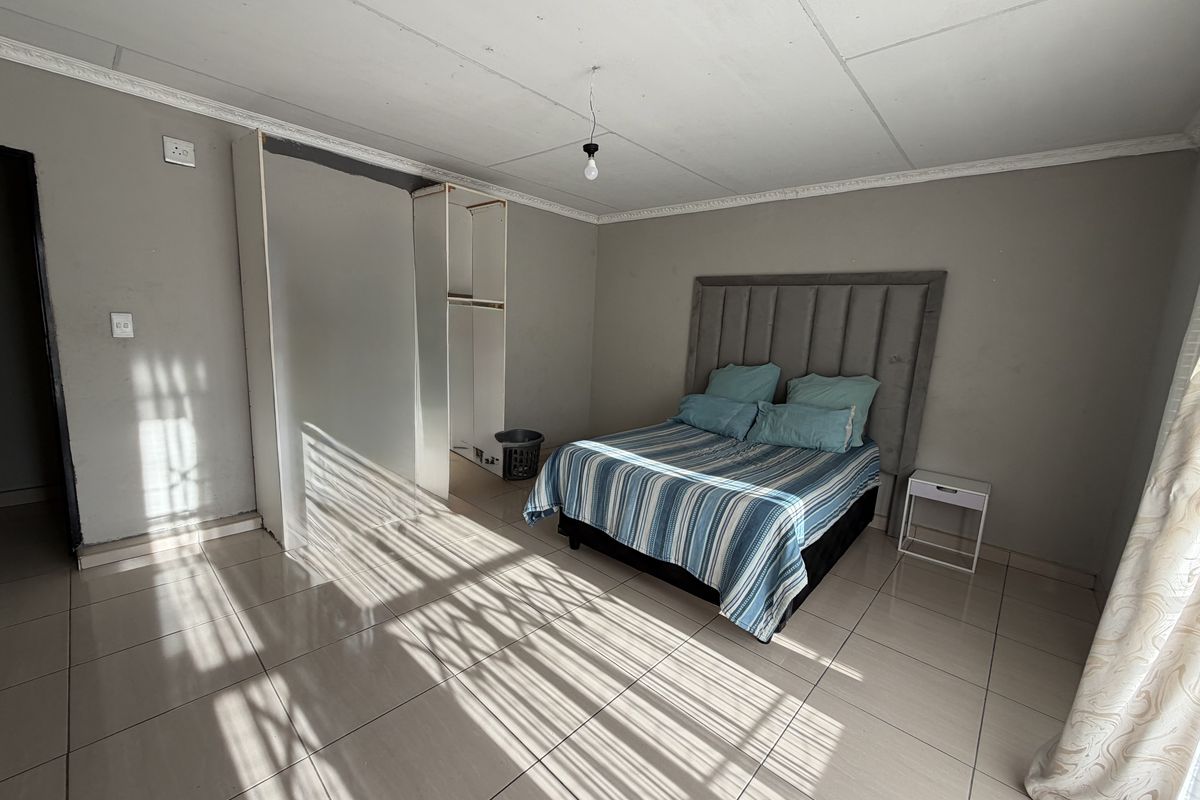 A bedroom featuring tiled flooring, built-in wardrobe storage, and decorative ceiling cornicing, requiring some maintenance to the ceiling finish.