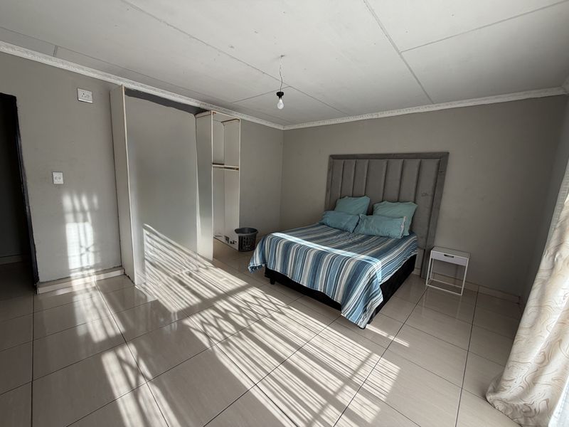 A bedroom featuring tiled flooring, built-in wardrobe storage, and decorative ceiling cornicing, requiring some maintenance to the ceiling finish.