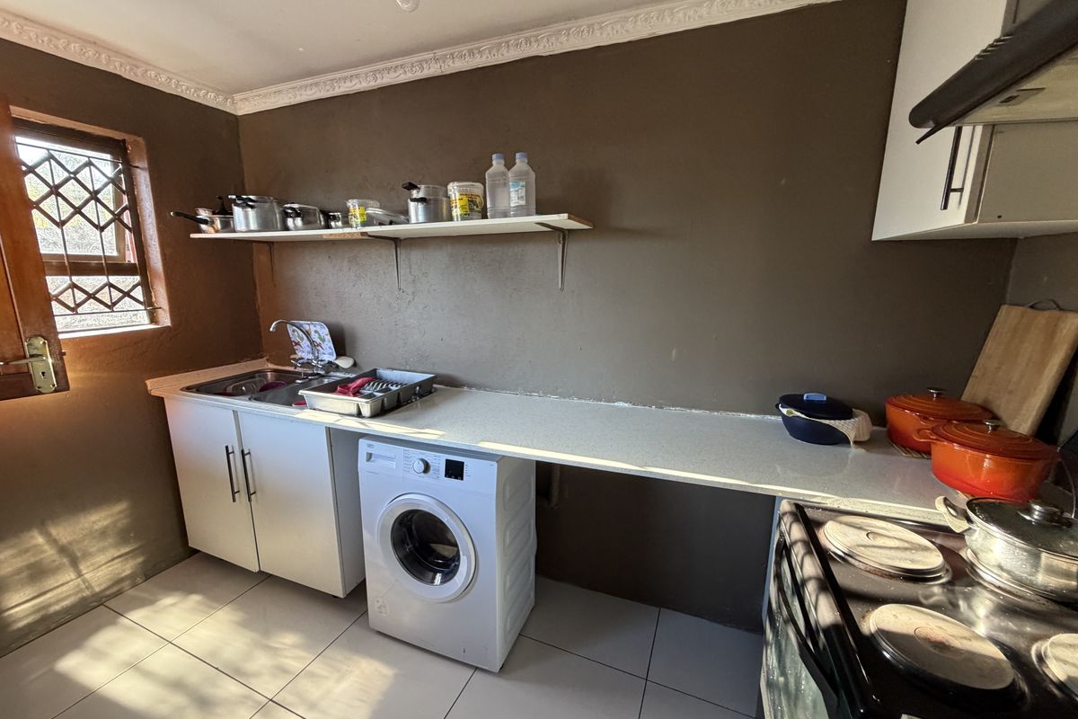 A functional kitchen featuring tiled flooring, built-in cabinetry, a stainless steel sink, and an electric stove with an extractor fan.