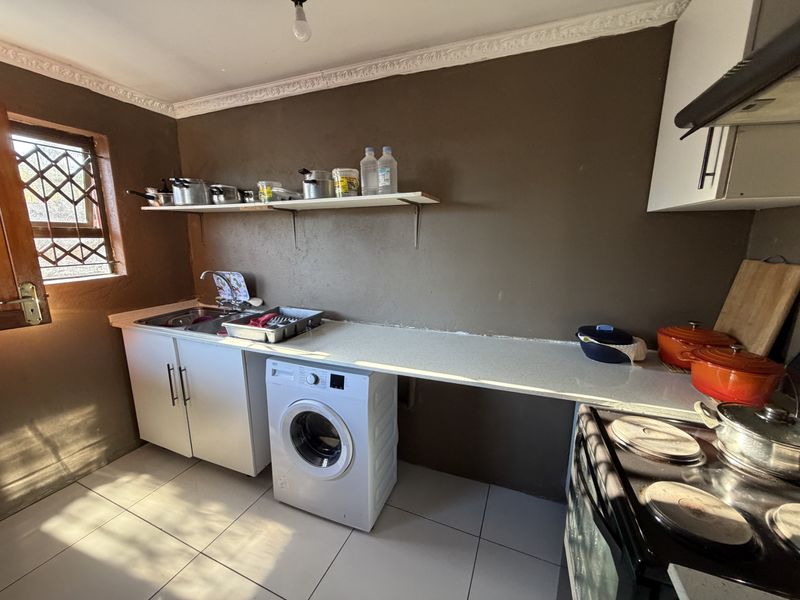 A functional kitchen featuring tiled flooring, built-in cabinetry, a stainless steel sink, and an electric stove with an extractor fan.