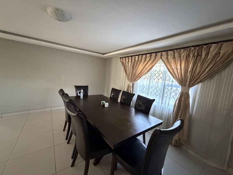 A dining room featuring tiled flooring and a recessed ceiling detail, with a security gate installed on the window.