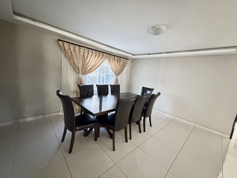 A bright dining room featuring neutral walls, large format floor tiles, and a decorative recessed ceiling detail.