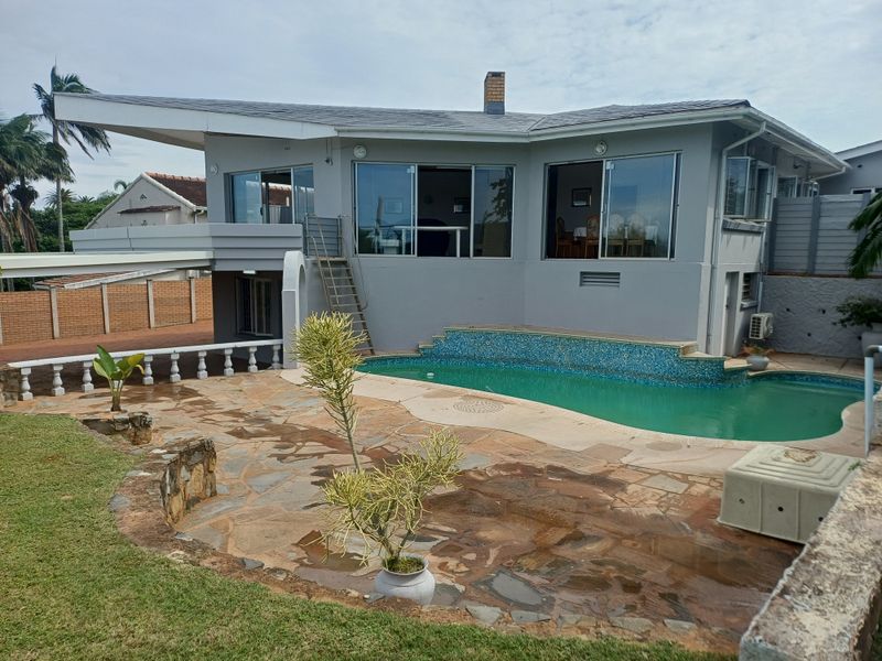 Rear exterior view featuring a swimming pool with mosaic tile detail, a stone-paved patio area, and access to the main living level via sliding doors.